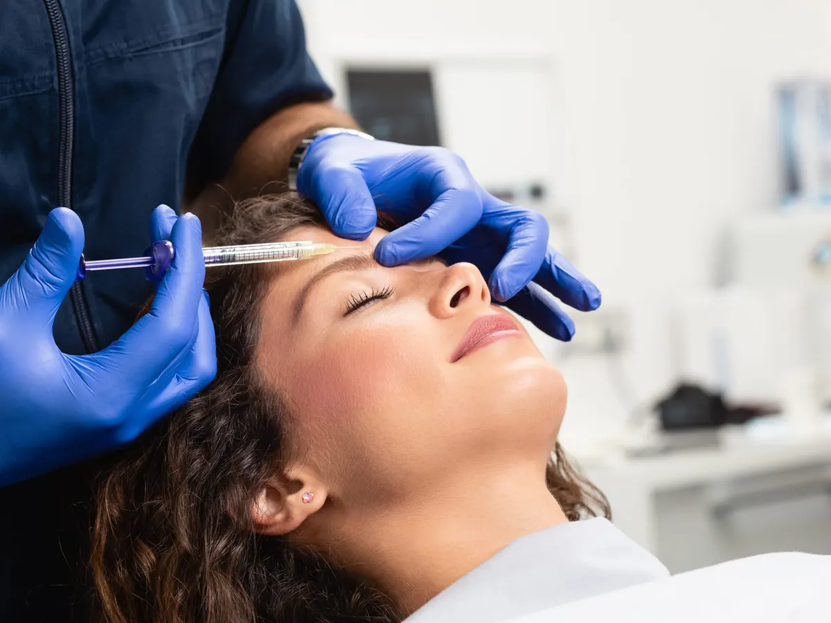 Gloved hands giving an injection in a woman's forehead