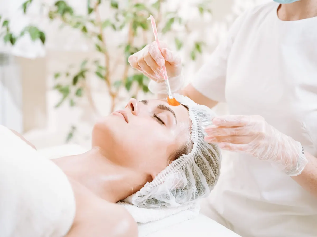 A provider brushes a chemical peel solution onto a relaxed patient’s face