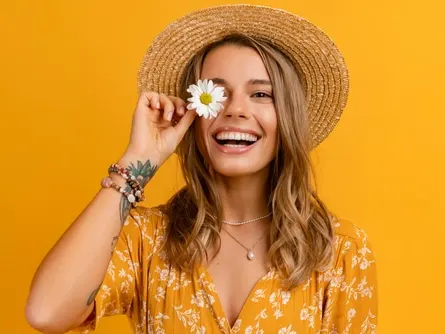 attractive stylish woman in yellow dress and straw hat holding daisy flower