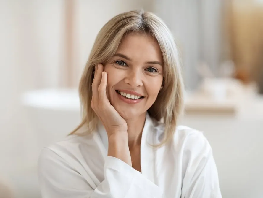 Smiling older woman touching her face and showing off her smooth, fresh skin after Photofacial.