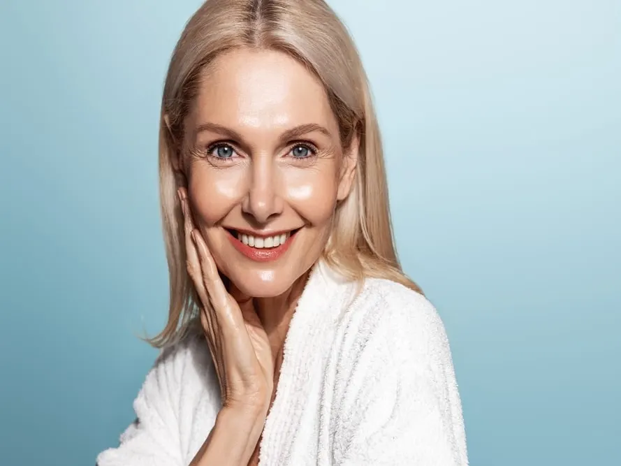 A woman smiling and touching her cheek after Fractora for skin rejuvenation