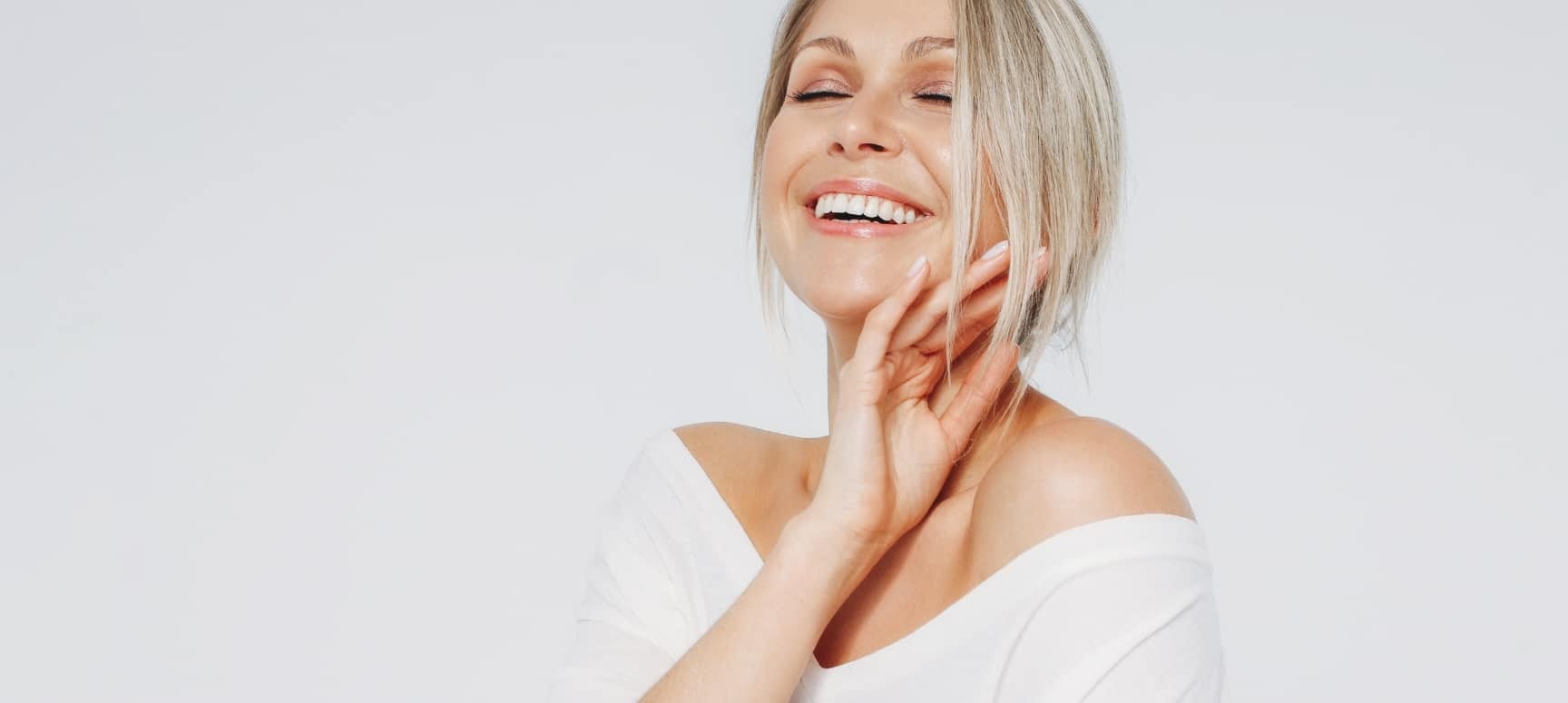Smiling woman with her eyes closed, touching her face and neck
