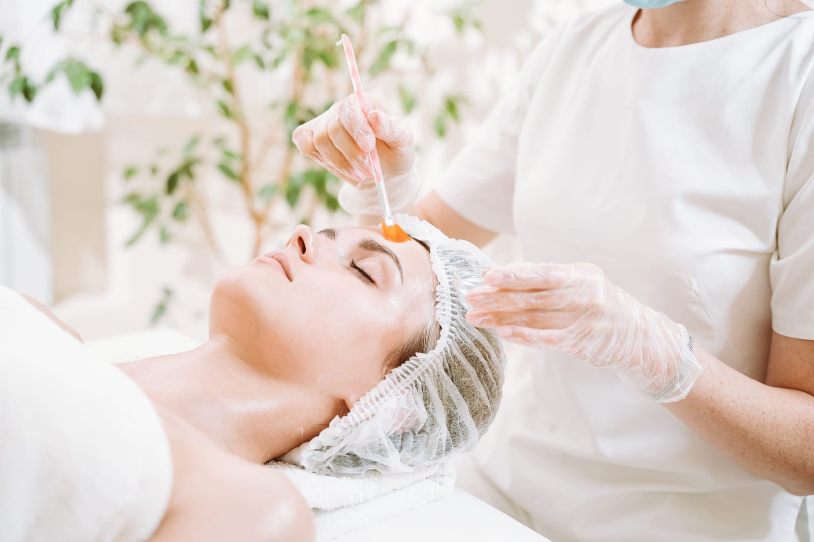 A provider brushes a chemical peel solution onto a relaxed patient’s face