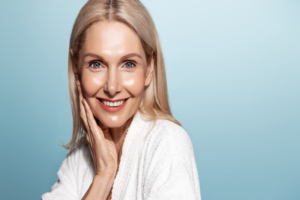 A woman smiling and touching her cheek after Fractora for skin rejuvenation