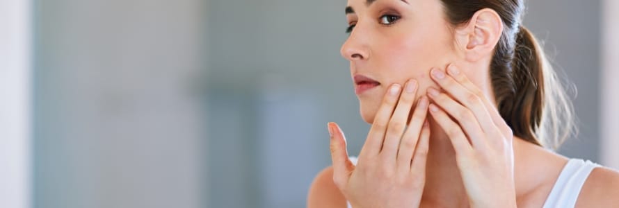 young woman looking at pimple in mirror