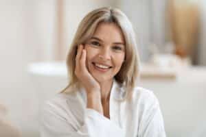Smiling older woman touching her face and showing off her smooth, fresh skin after Photofacial.