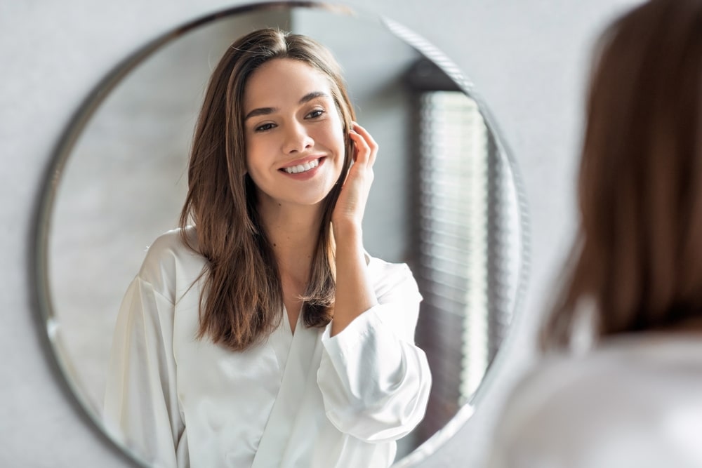 A woman looking in the mirror at the results of a liquid facelift in San Antonio
